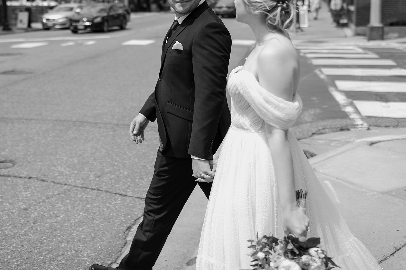 Close up of a bride and groom holding hands walking across the street