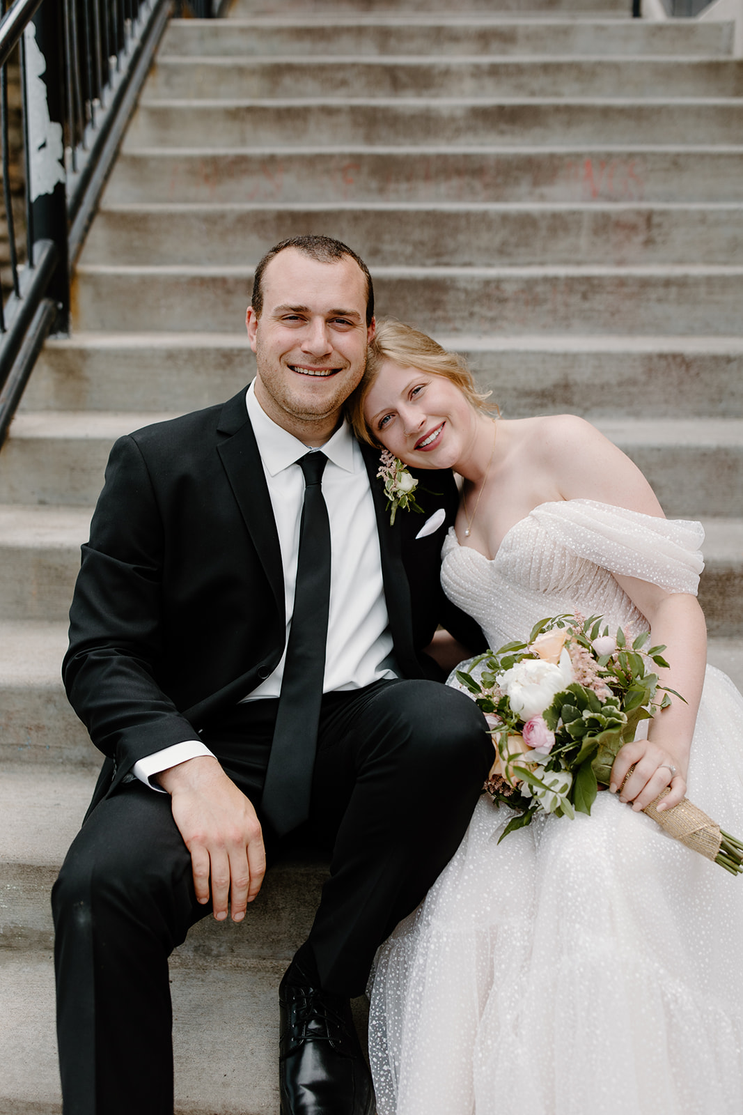 Bride and groom sitting on a staircase smiling at the camera