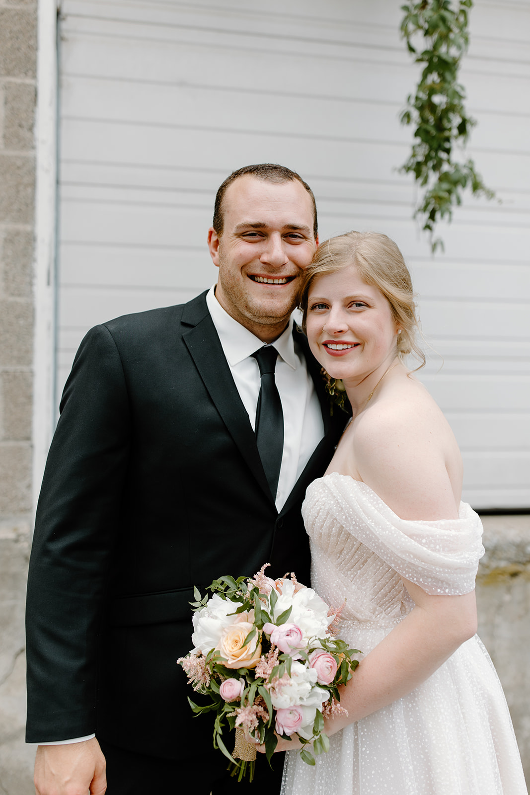 Bride and groom smile at the camera in front of a garage door