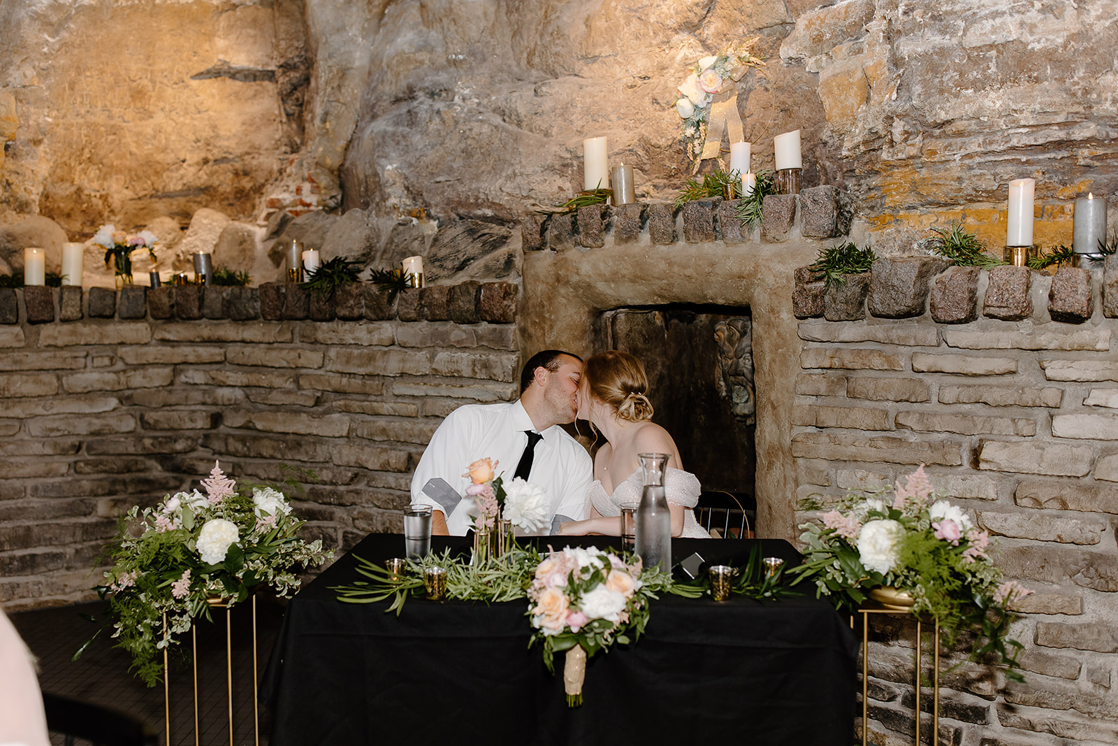Bride and groom kiss while sitting at their reception table at their wedding in a cave 