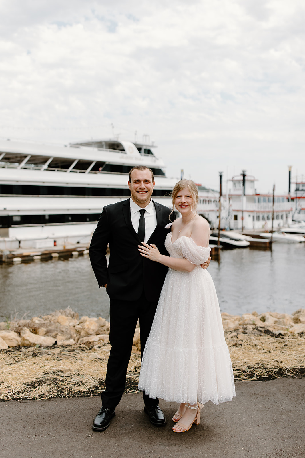 Bride and groom smile at the camera in front of a yacht