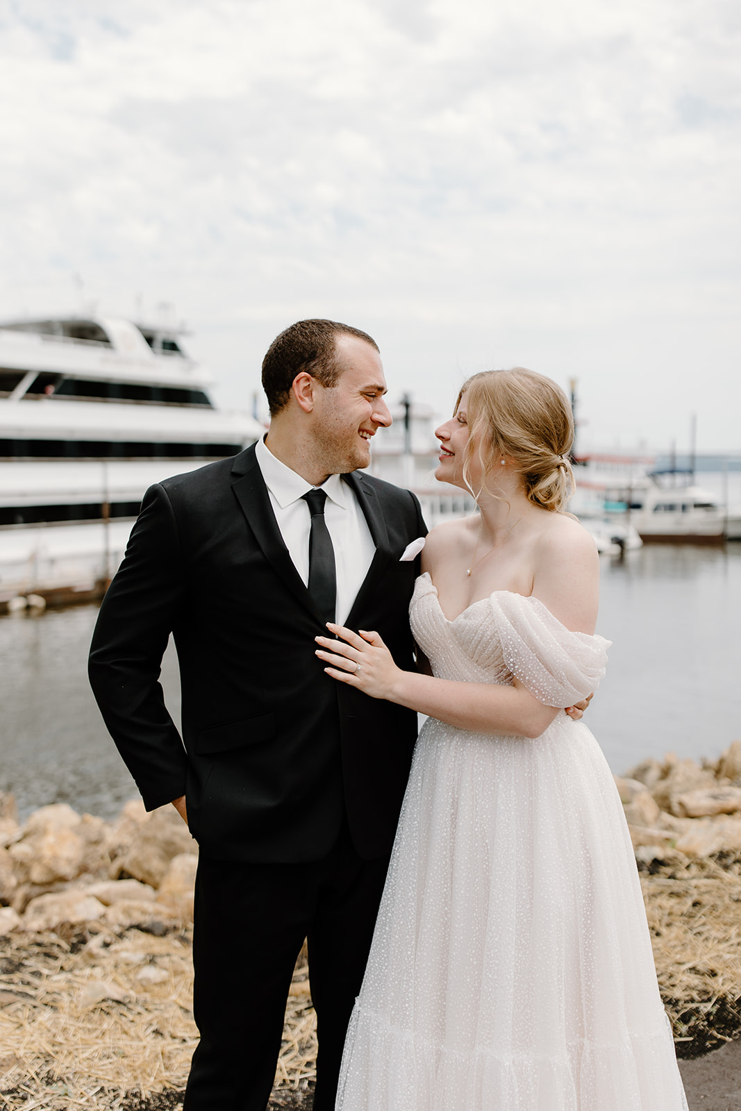 Bride and groom smile at each other in front of a yacht