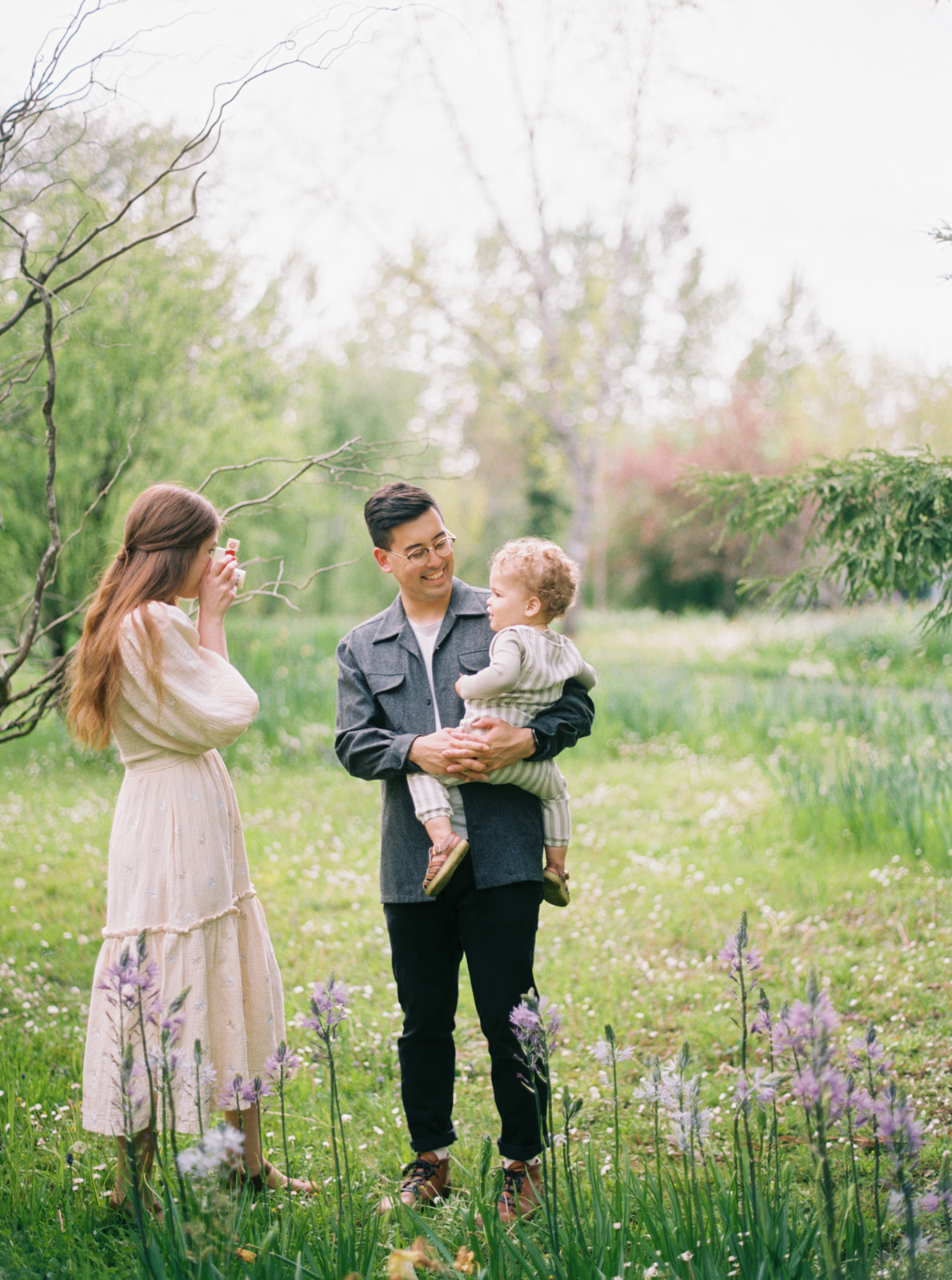 a young family plays with a toy camera in wildflowers