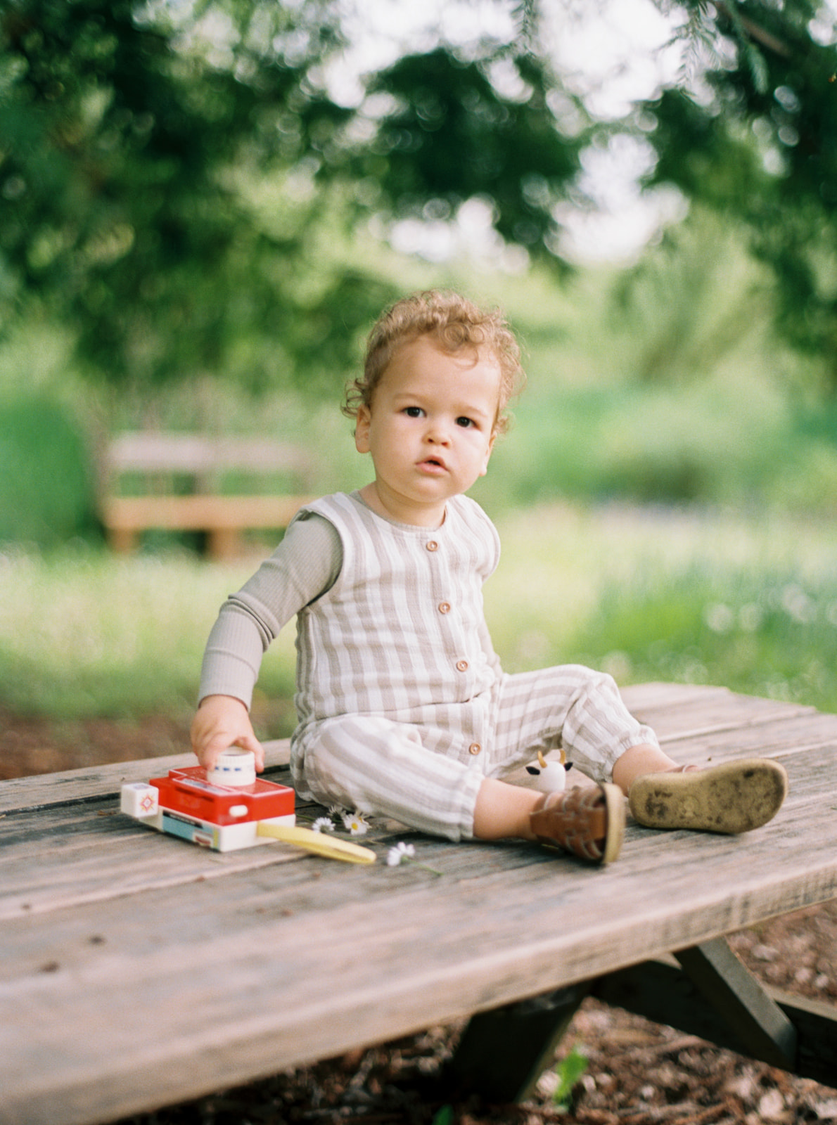 toddler sits on picnic table with retro toy camera