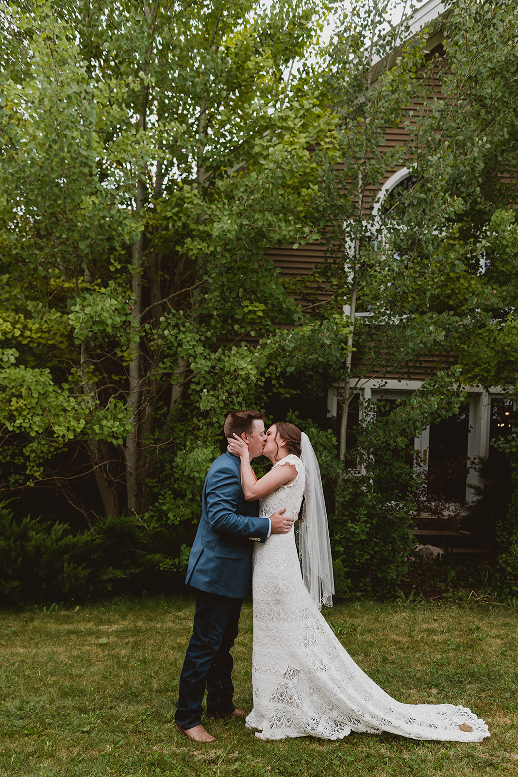 Couple kiss in a lush backyard in their wedding attire at their wedding in Steamboat Springs, CO
