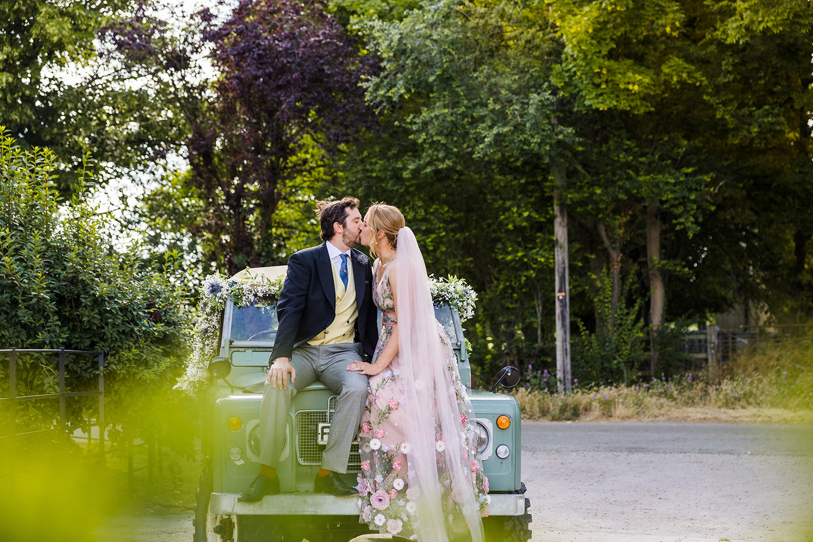 A wedding couple sitting on an antique landrover kissing