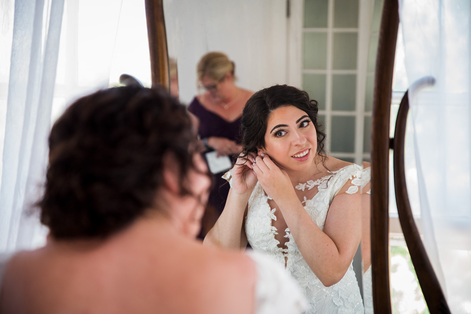The bride looks in the mirror as she puts on an earring and gets ready for her wedding.