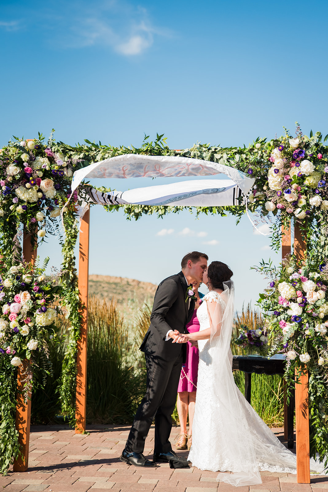 A bride and groom share their first kiss under a Jewish Chuppah covered in flowers. 