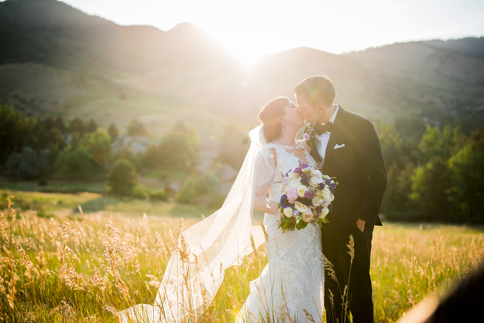 The bride and groom share a kiss in a golden field with the sunset behind them.