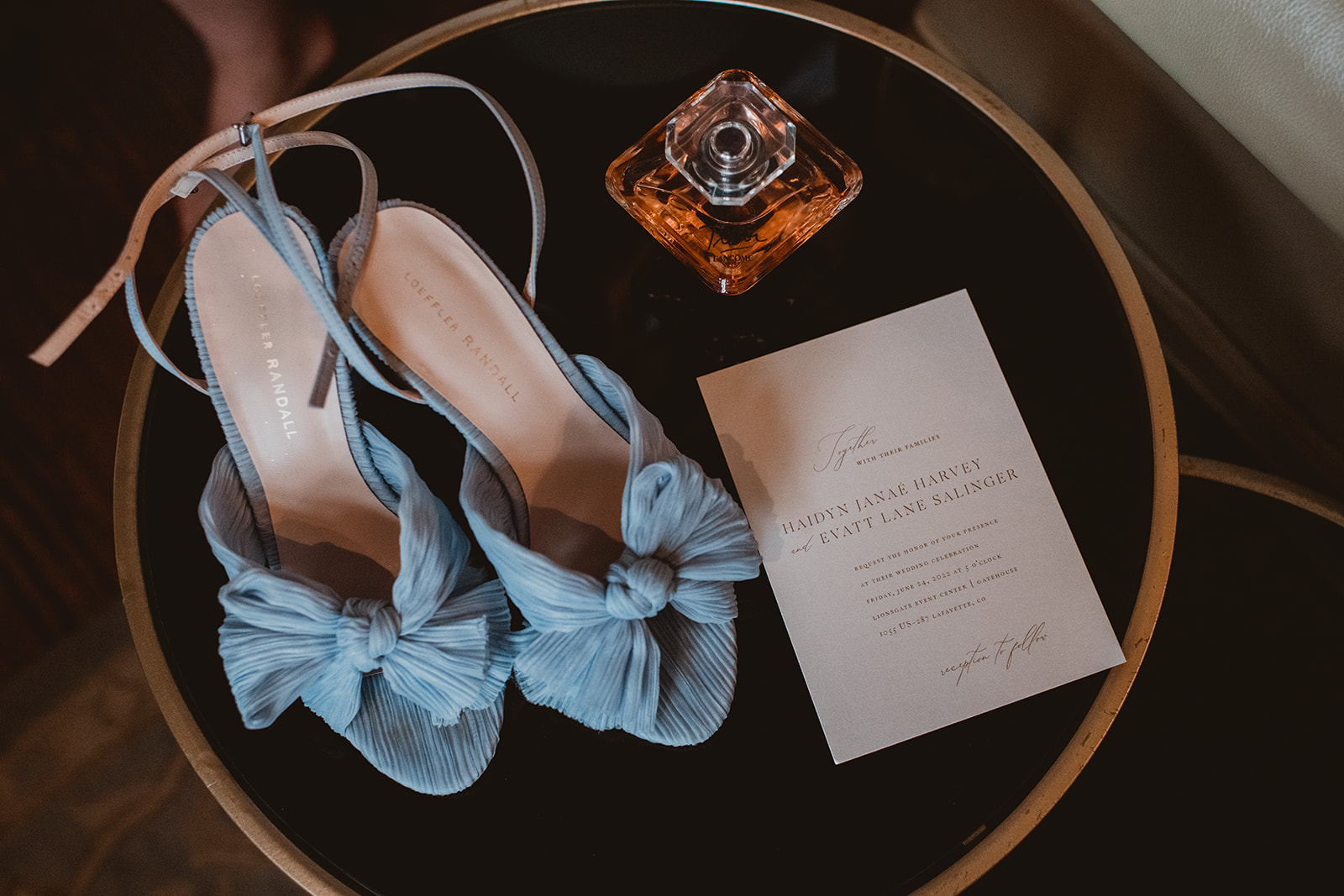 Blue heels sit next to wedding invite and perfume 