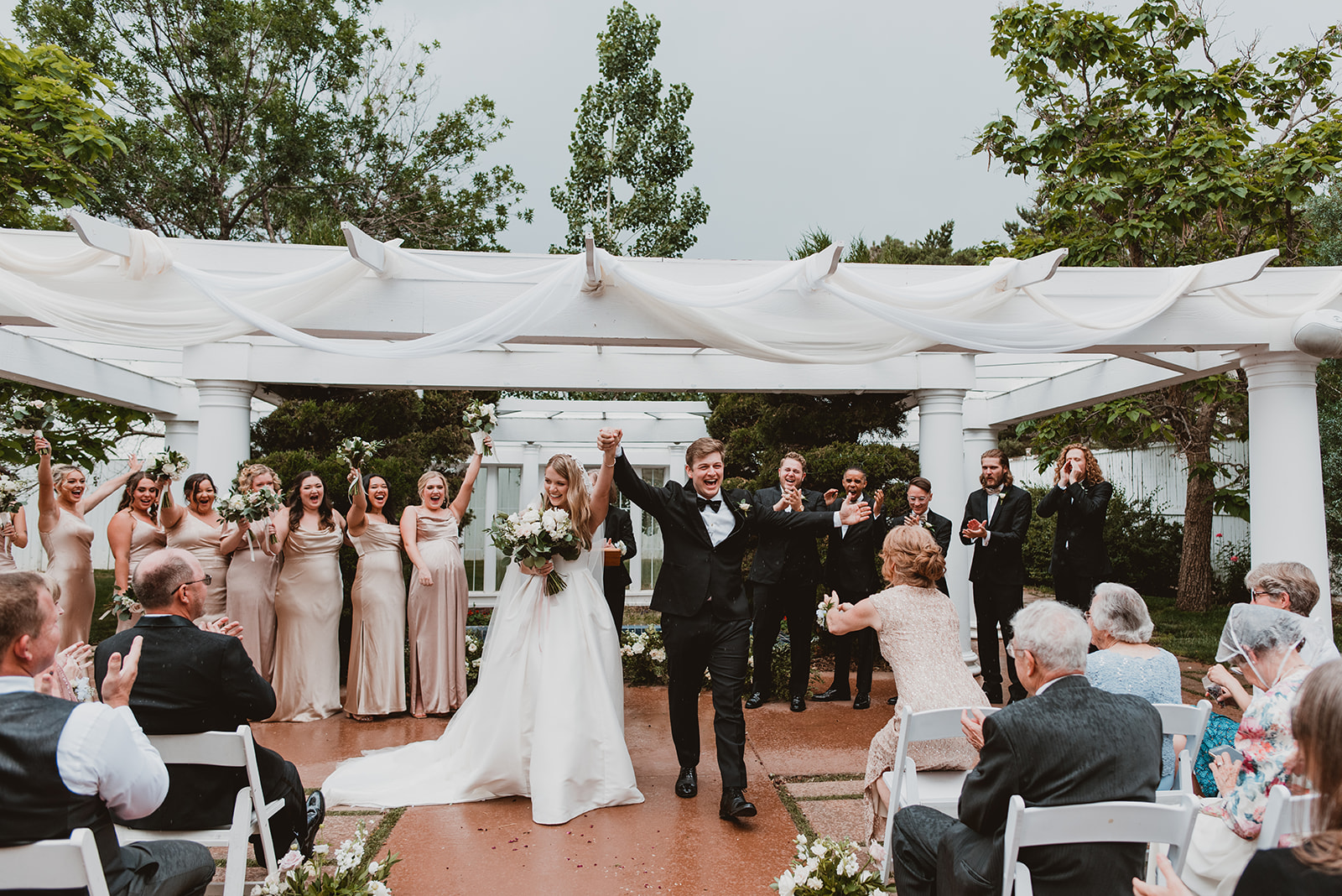 Bride and groom celebrate while walking away from a white gazebo on their wedding day after getting married in Denver CO