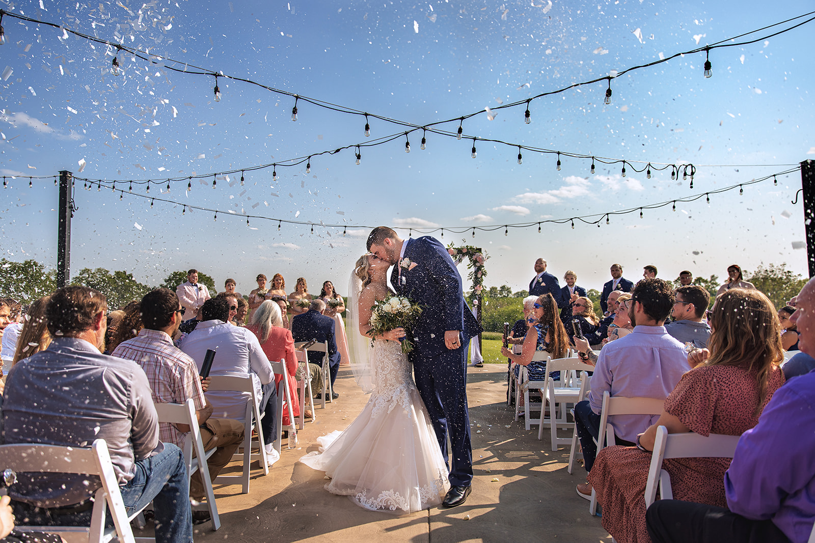 Bride and groom first kiss while guests fire confetti poppers at Bryton Barn