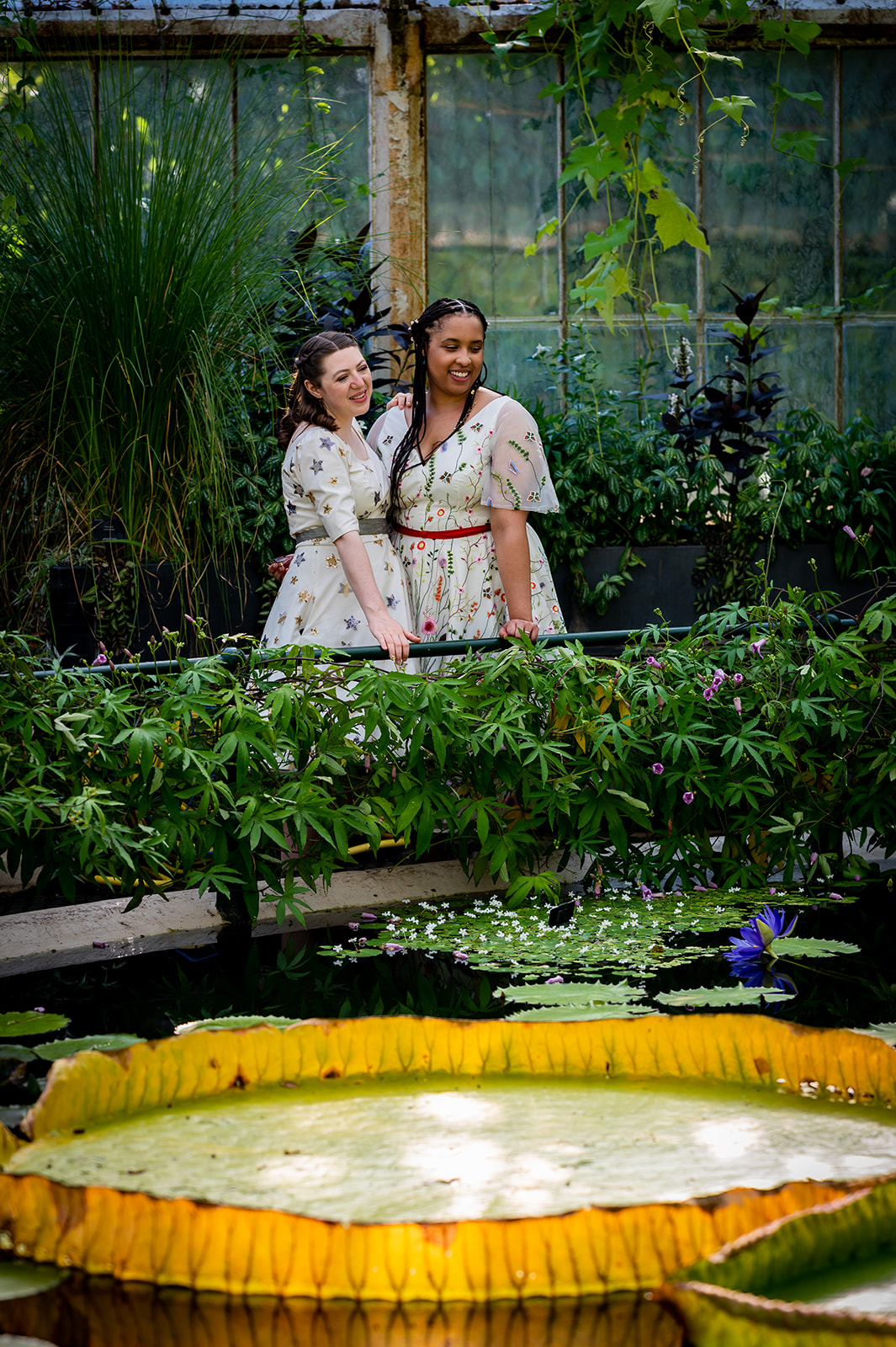 Two brides standing in front of a giant  Lily at the Lily House at Kew Gardens on their wedding day.
