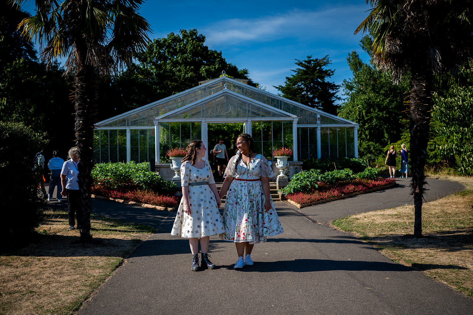 Two brides standing in front of the Lily House at Kew Gardens on their wedding day.