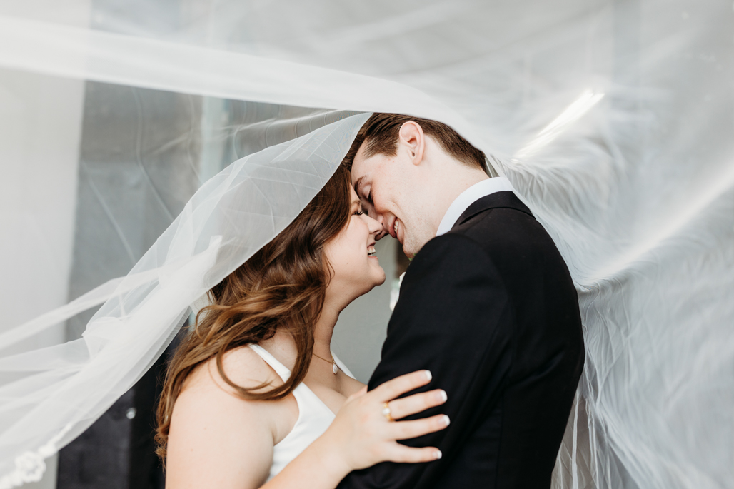 BRIDE AND GROOM SHARE ROMANTIC KISS UNDER VEIL AT MELLWOOD ARTS CENTER