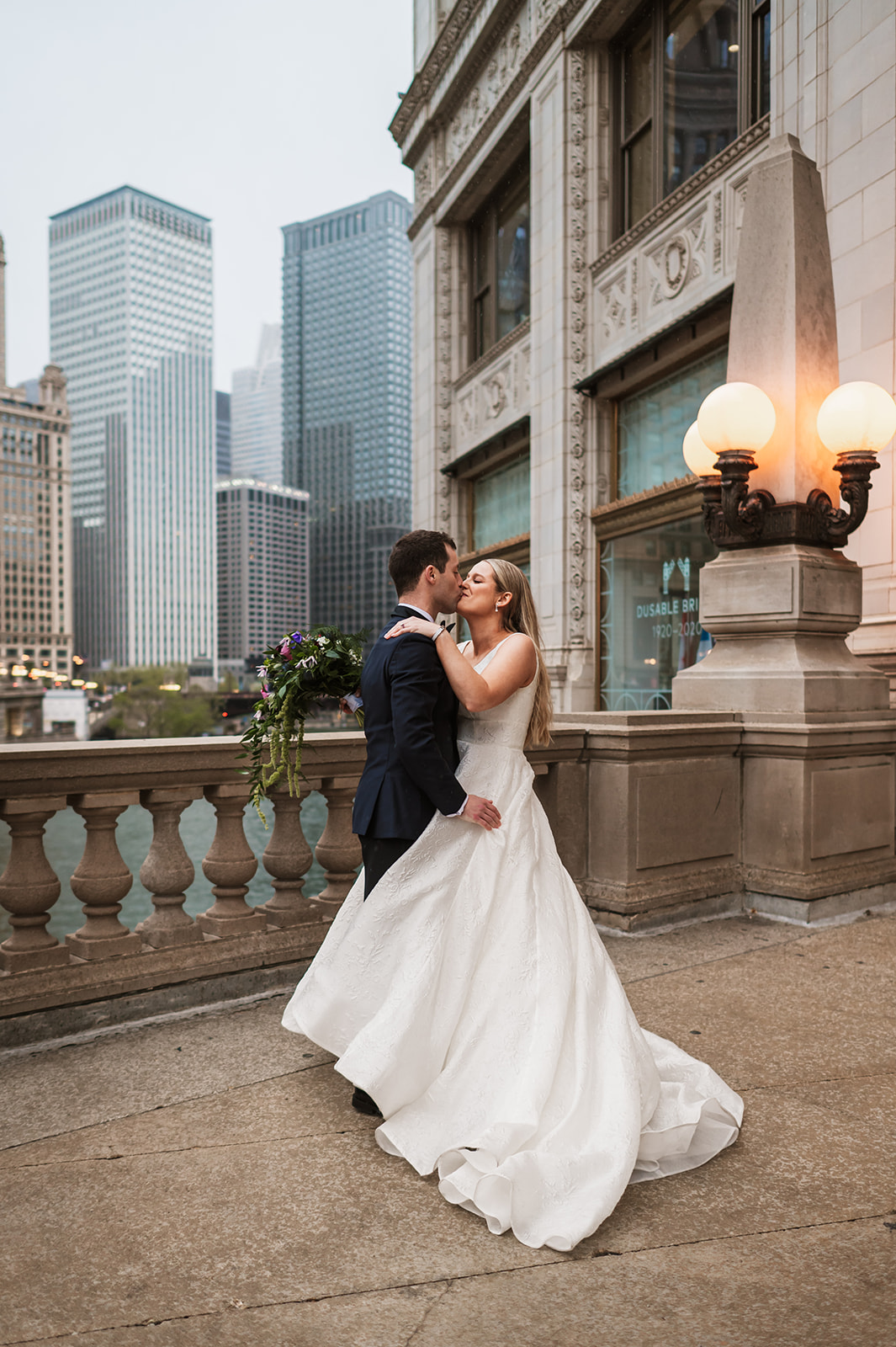 Bride running and jumping on a groom at the end of the winter on riverwalk by the Wrigley building chicago