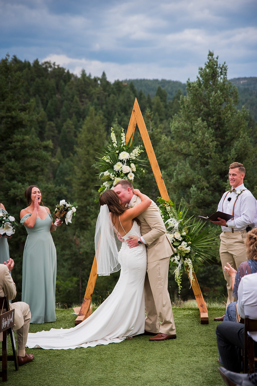 Bride and groom share their first kiss after the ceremony under a pointed wooden arch.
