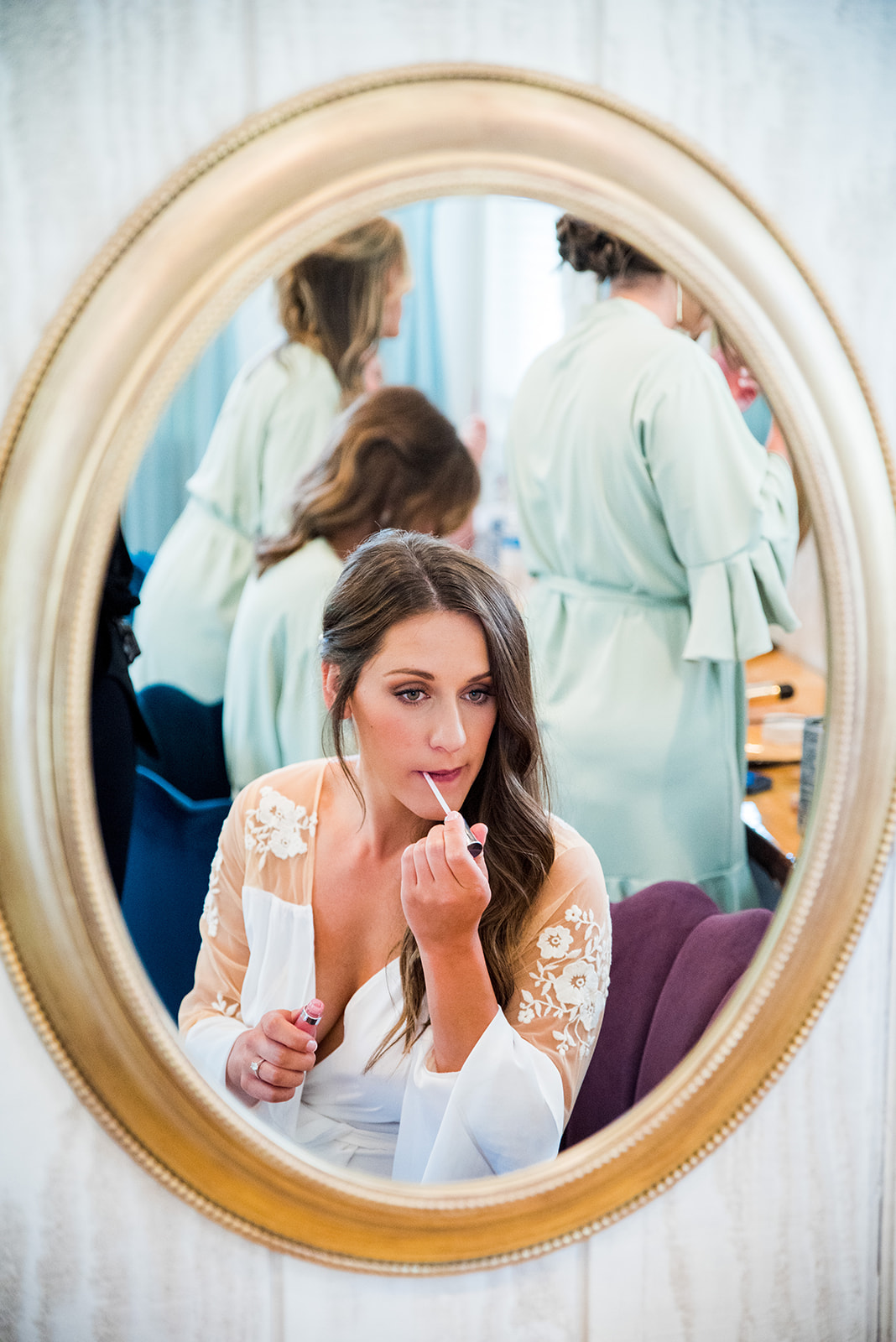 Bride looks in ornate gold mirror and applies finishing touches on her make up.