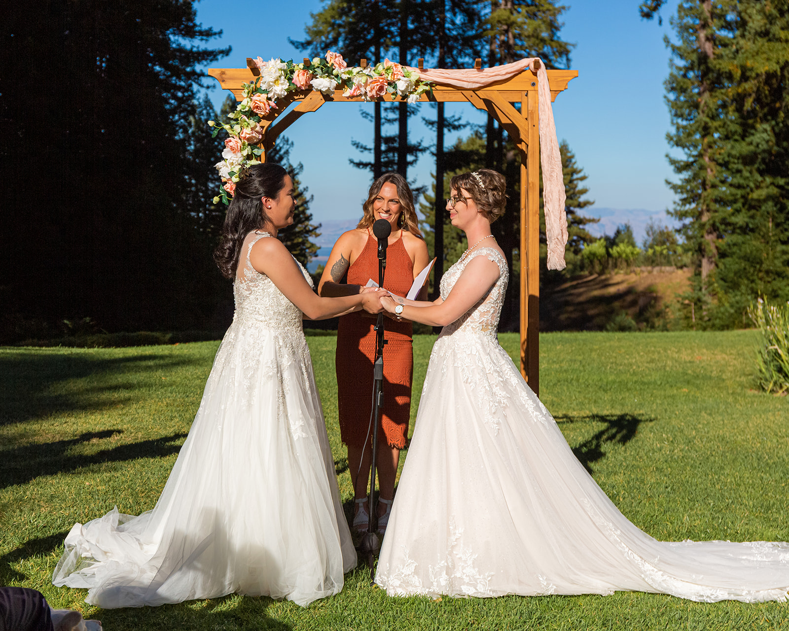 two brides in wedding dresses share vows in the redwoods