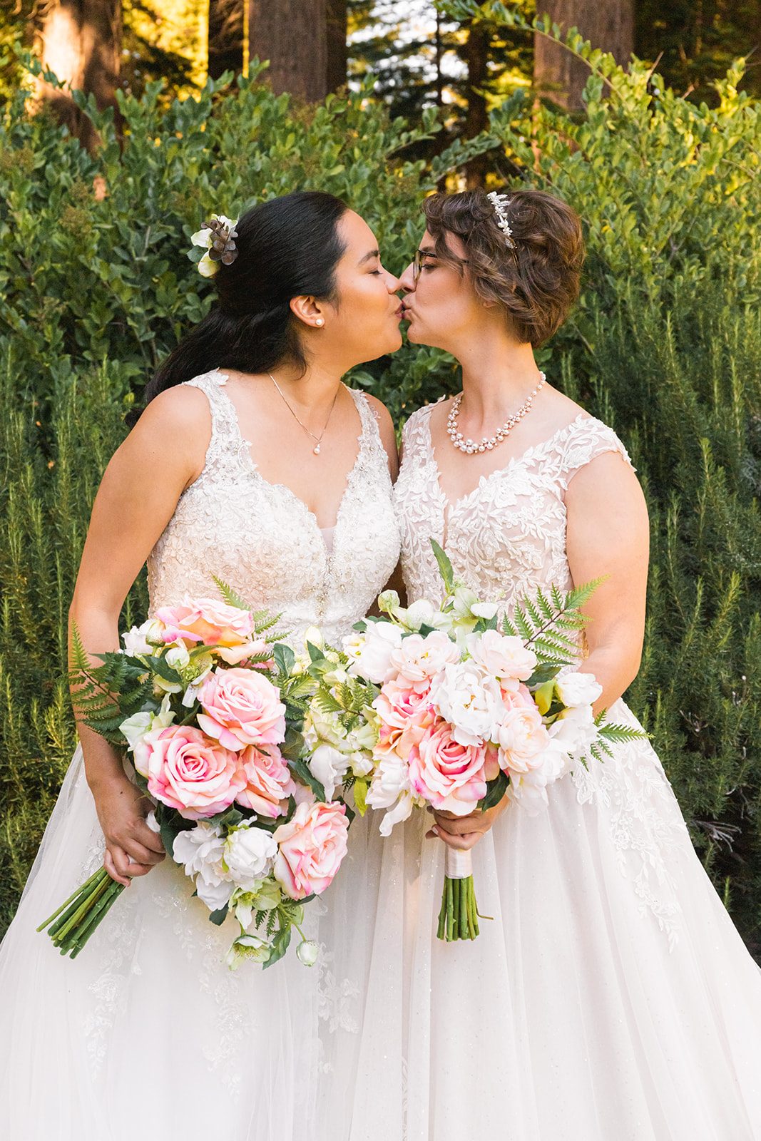 two brides in wedding gowns kissing while holding pink bouquets