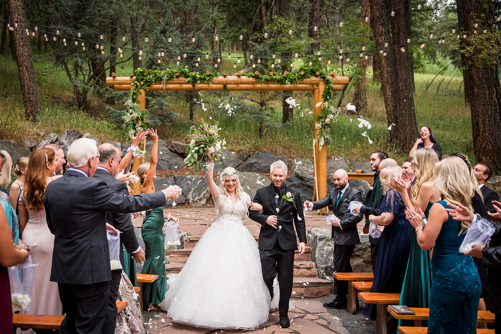 Bride and groom exit wedding ceremony hand in hand as audience celebrates by throwing petals. 