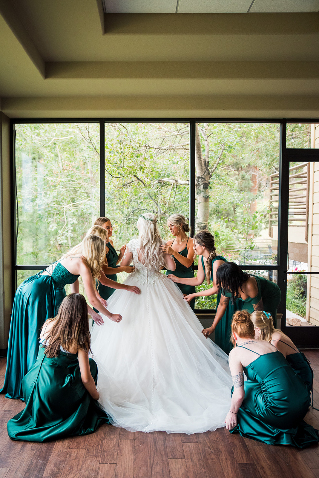 Brides faces window as her bridesmaids fluff her dress.