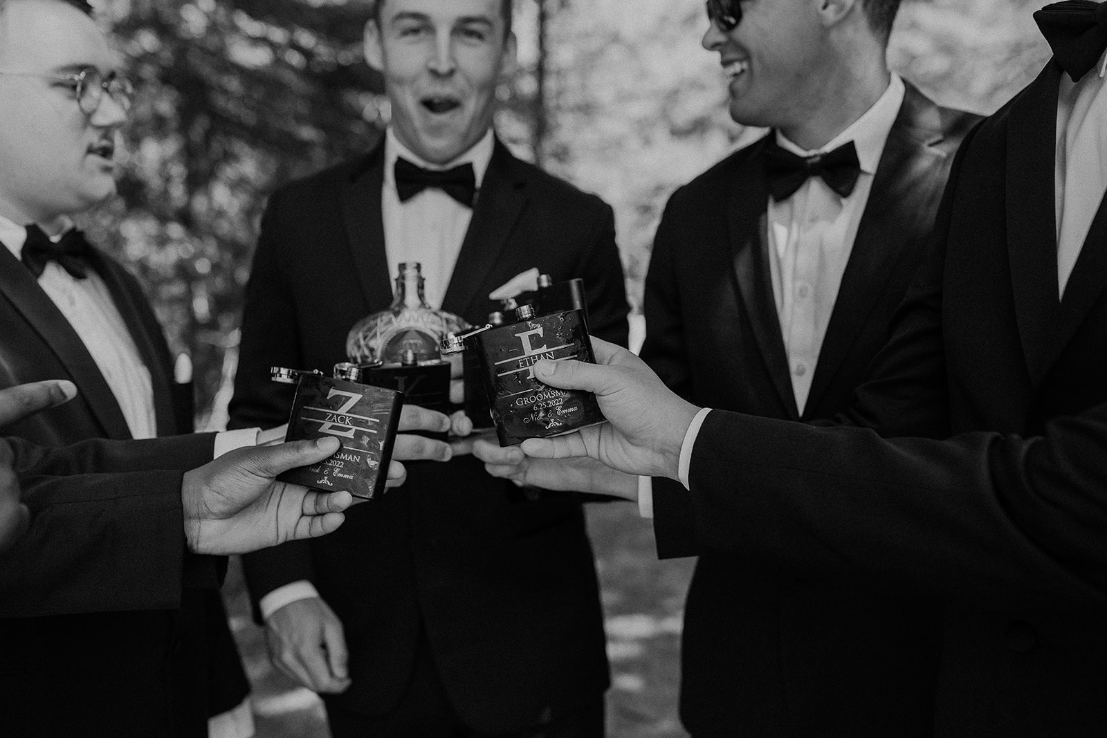 Groom and groomsmen sharing a drink and laugh before the wedding with custom wedding flasks at private lake house.