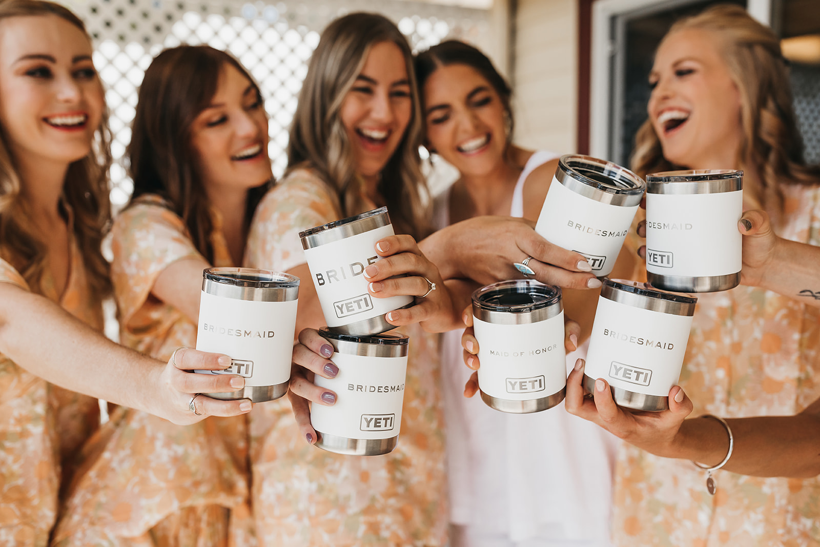 Bride and bridesmaids sharing a drink and laughs while getting ready with custom Yeti cups at private lake house.