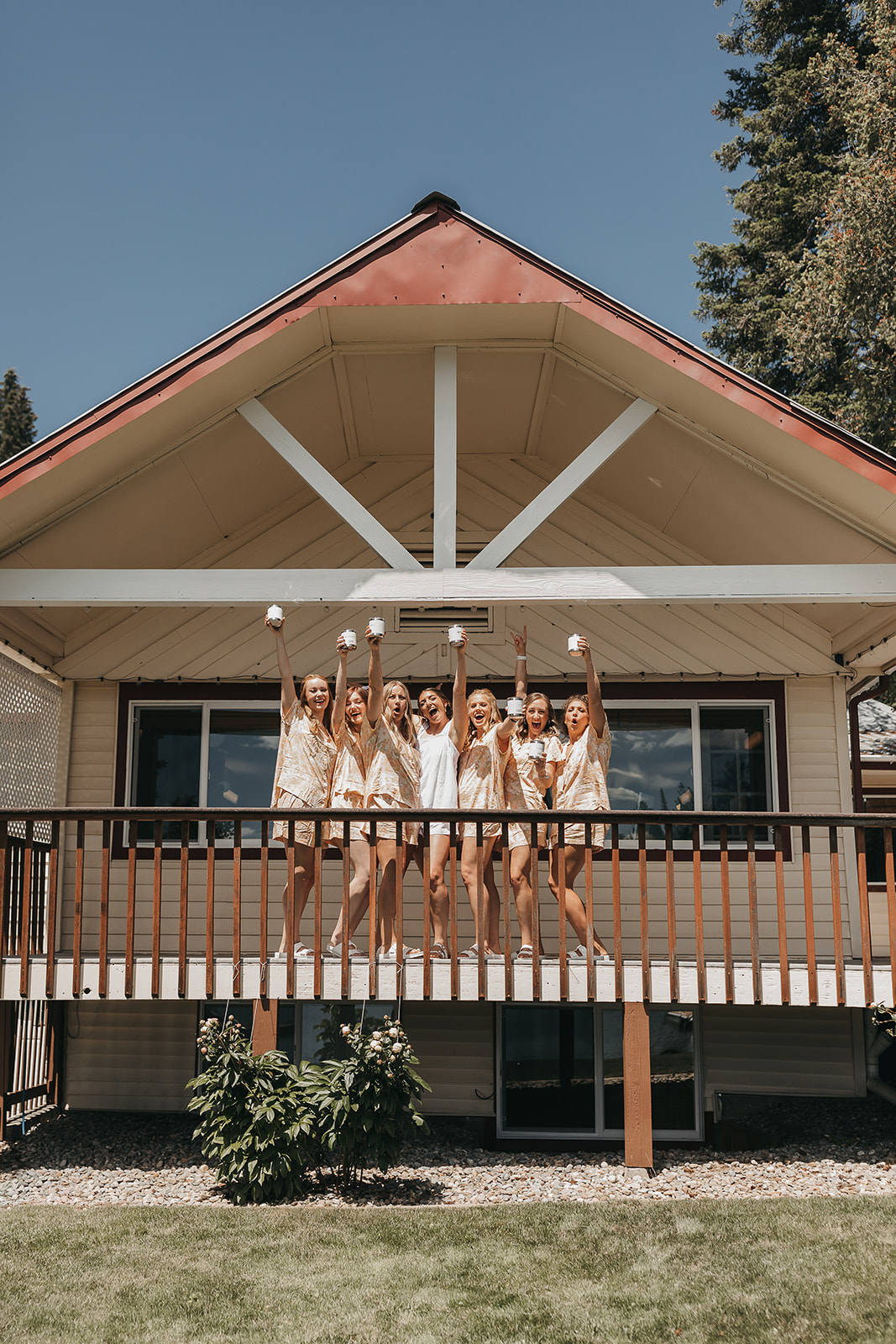 Bride and bridesmaids sharing a drink and laughs while getting ready with custom Yeti cups at private lake house balcony