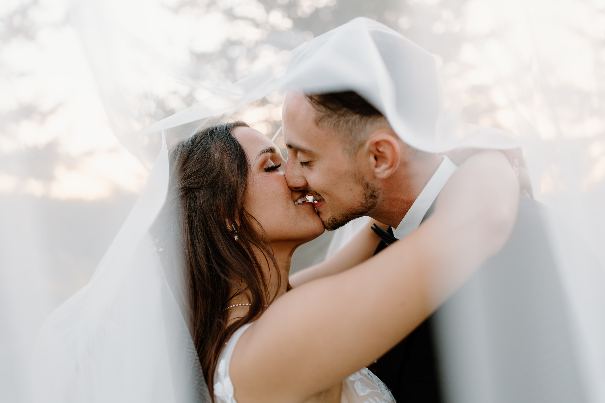 Bride and groom share a kiss underneath a veil