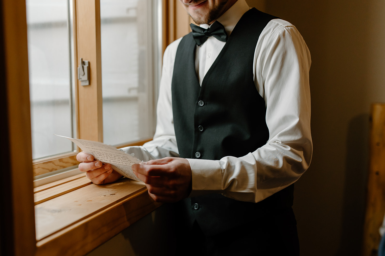 Groom reading a letter in front of a window
