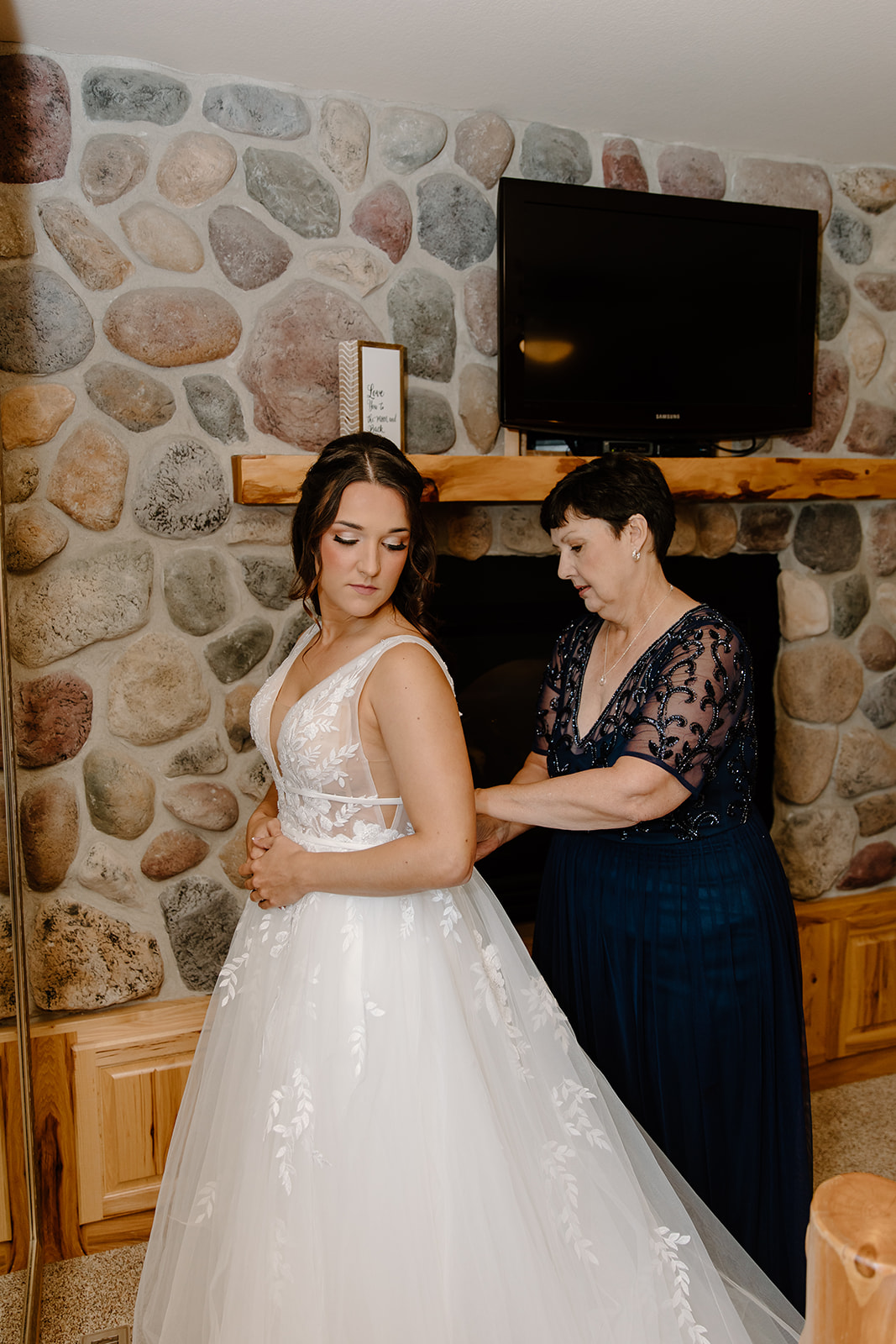 Mother zips up her daughter's wedding dress in front of a brick wall