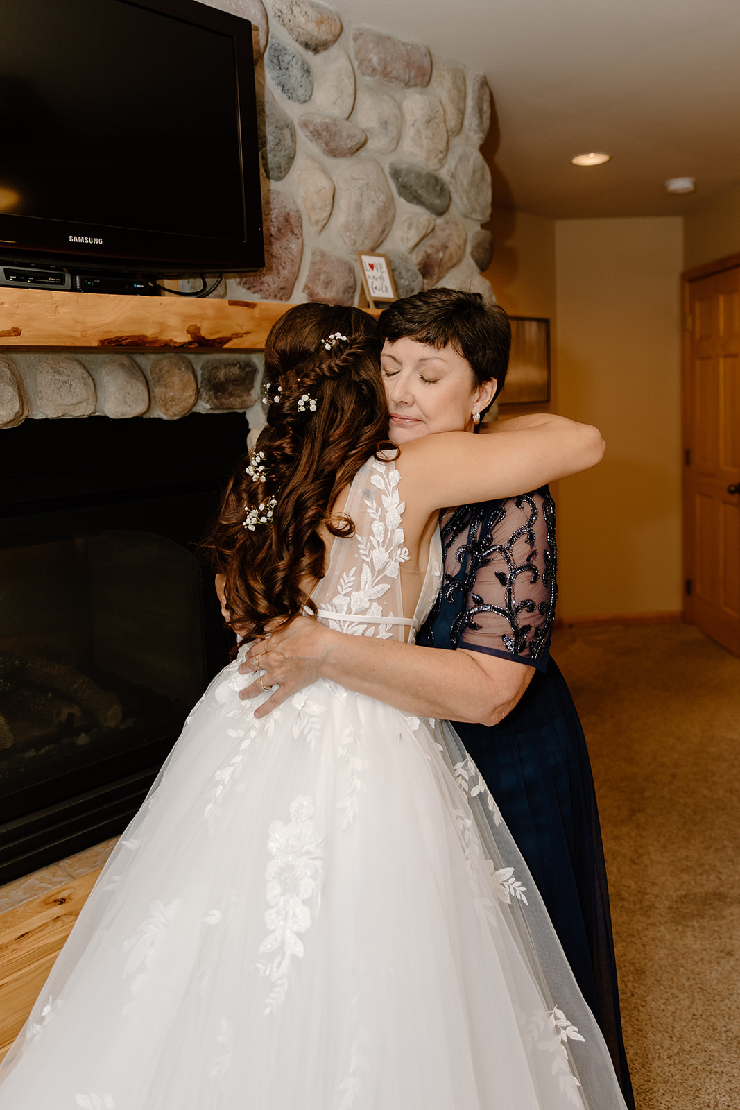 Bride hugs her mother in front of a brick wall 