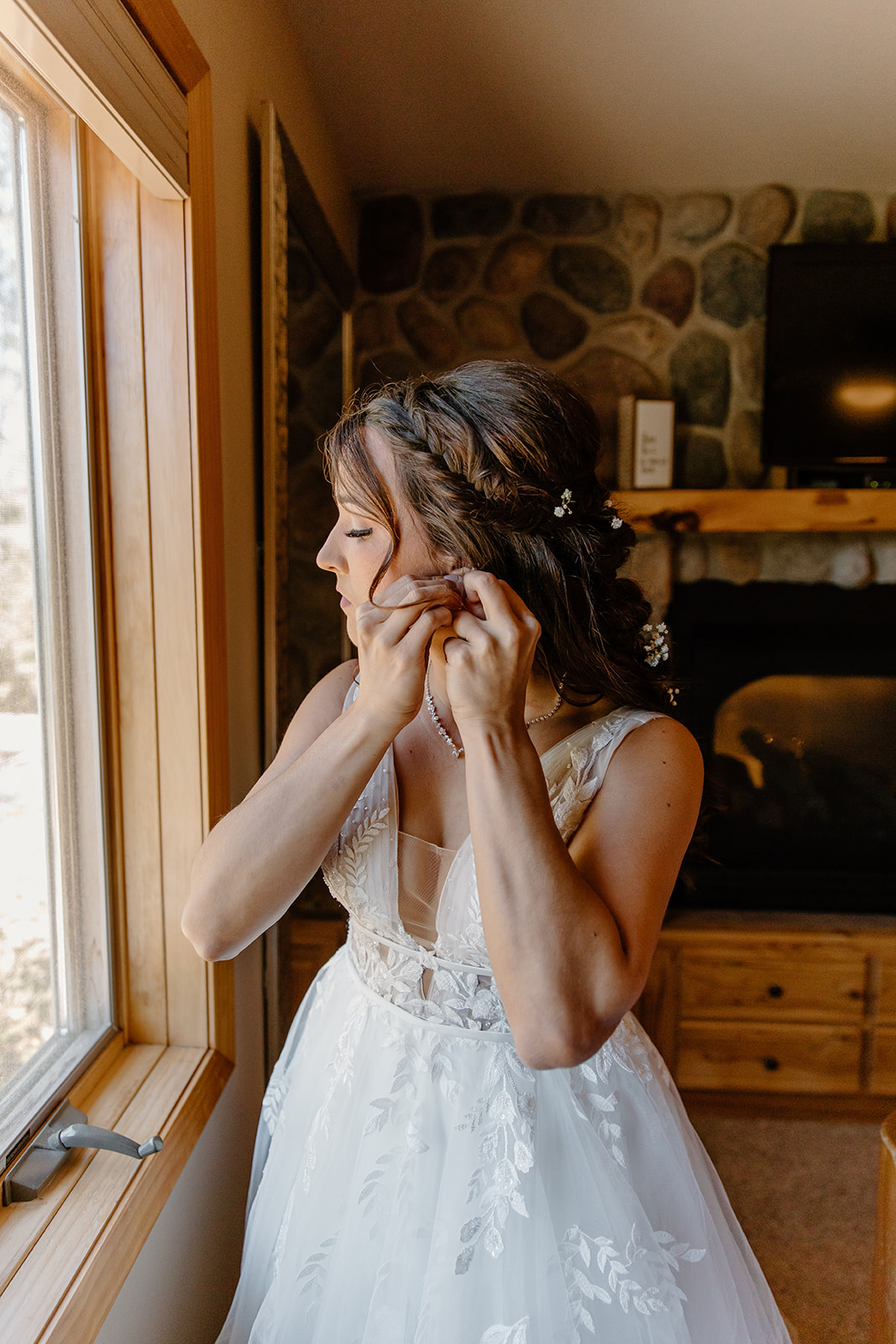 Bride puts in earrings in front of a window