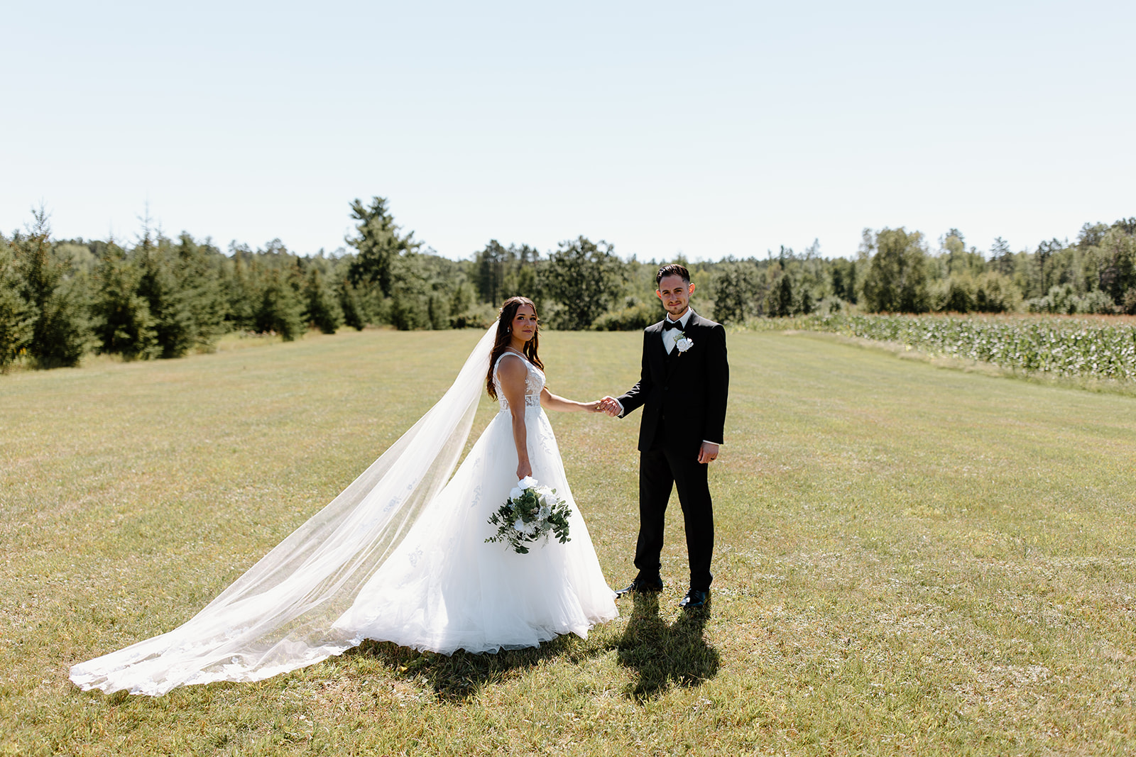Bride and groom hold hands in an open field
