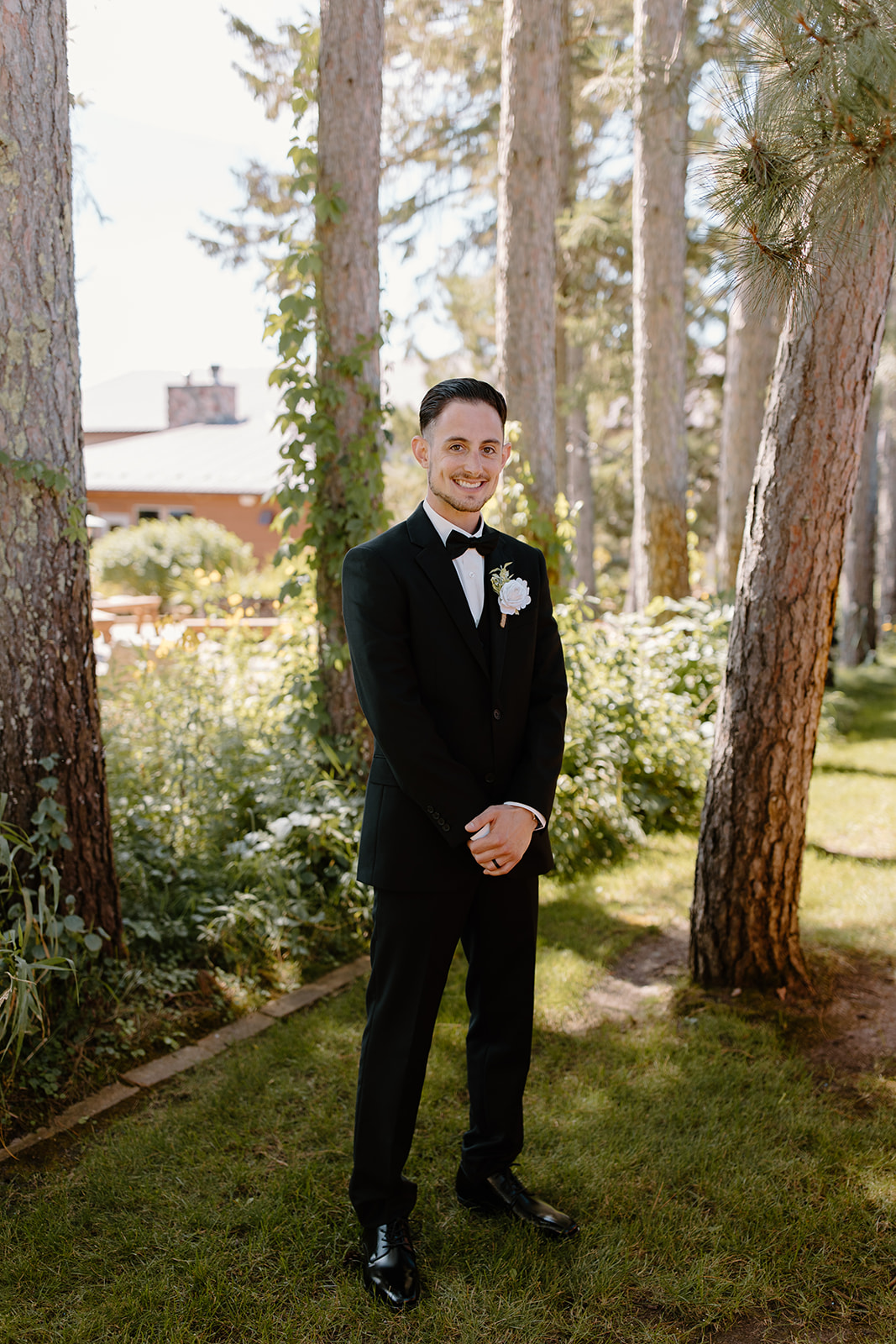 Groom smiles at the camera in front of a line of trees