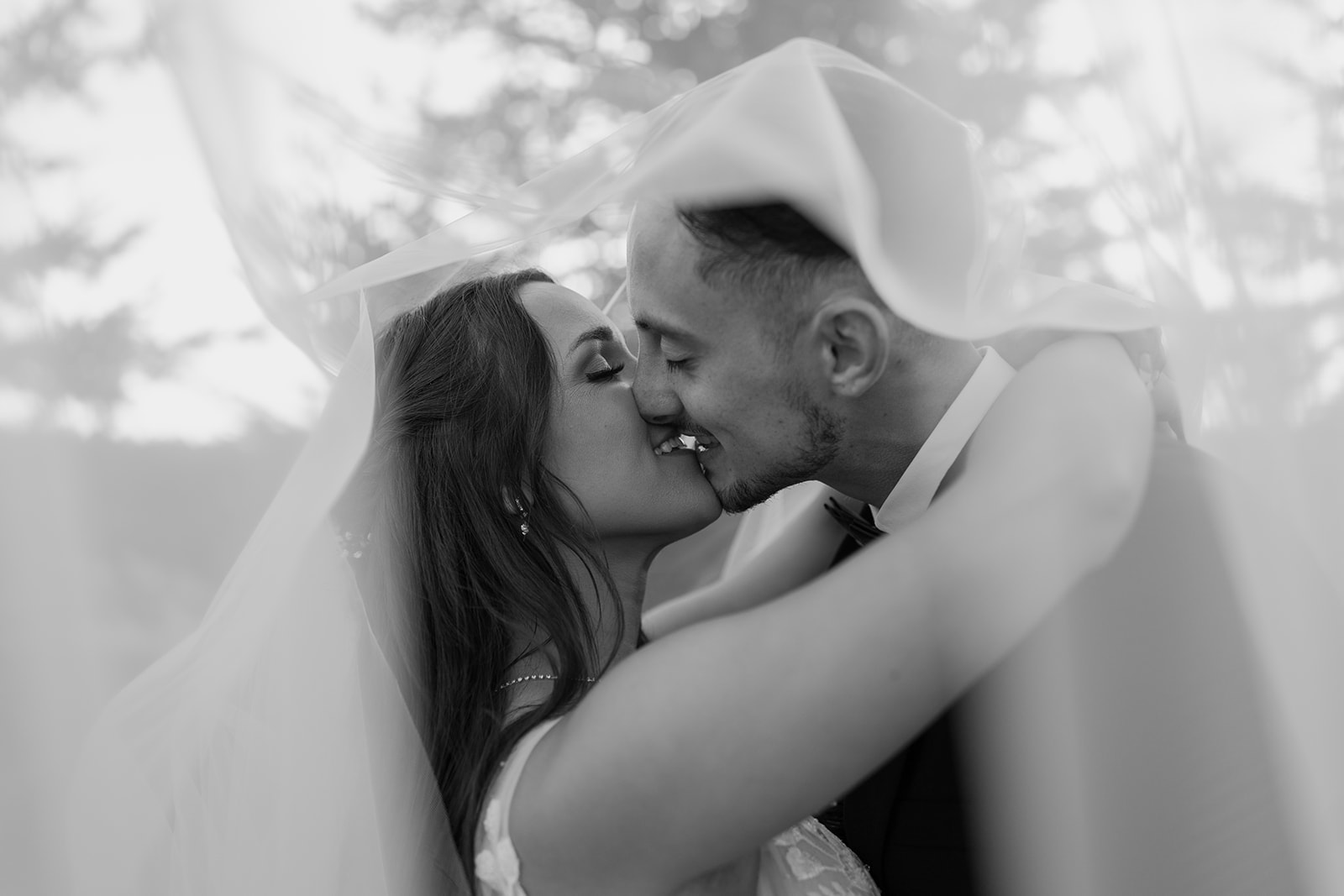 Bride and groom kiss underneath a veil
