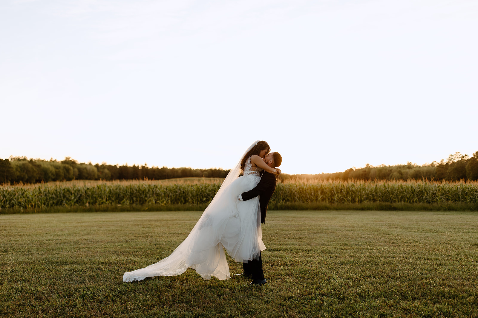 Groom lifts his bride in front of the sunset