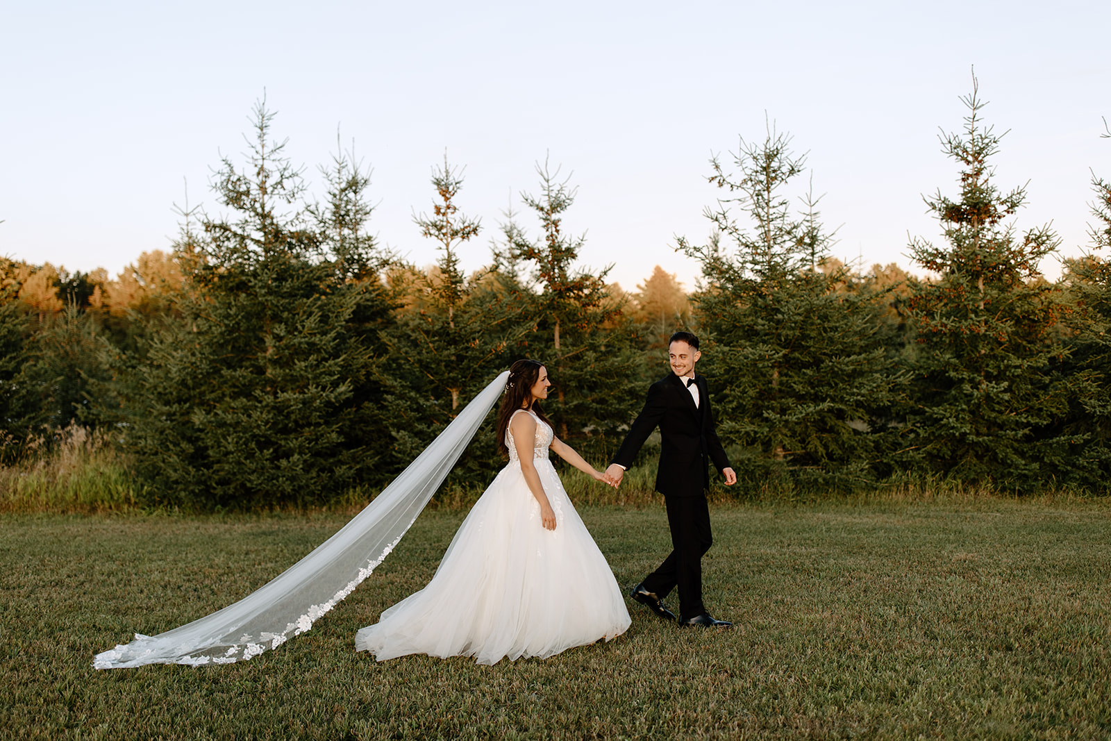 Groom leads his bride in front of a row of trees