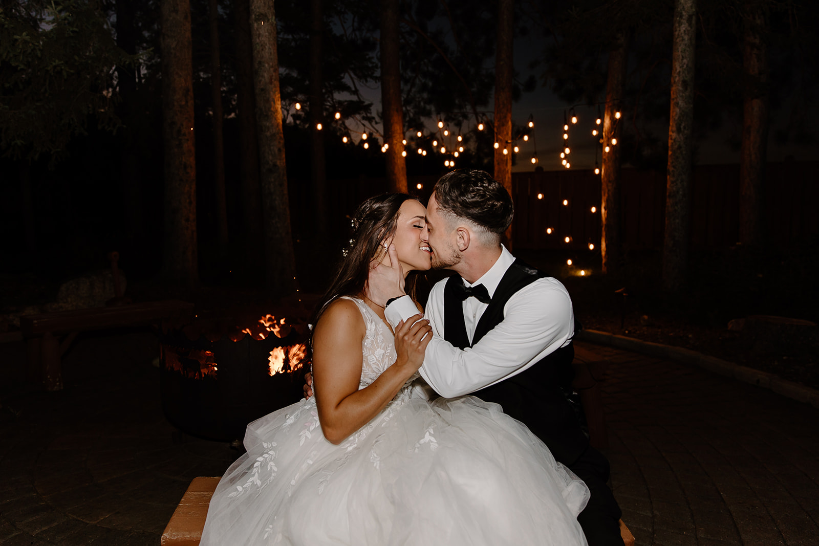 Bride and groom kiss in front of a fire pit