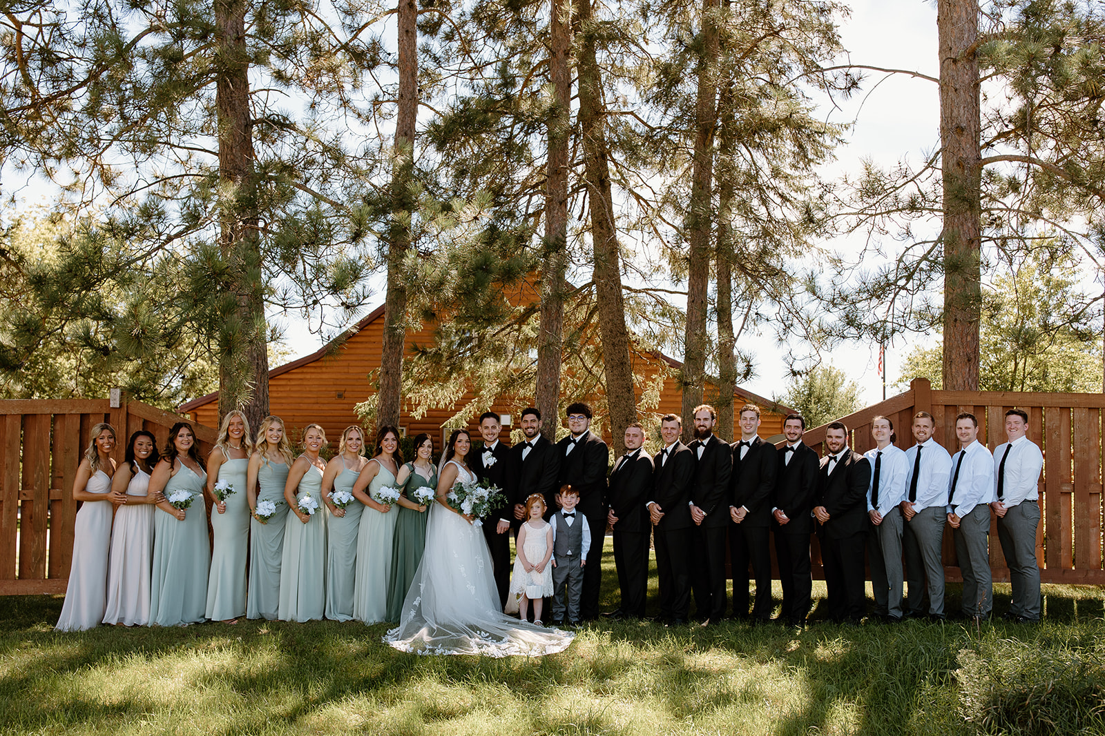 Wedding party smiles at the camera in front of a log cabin