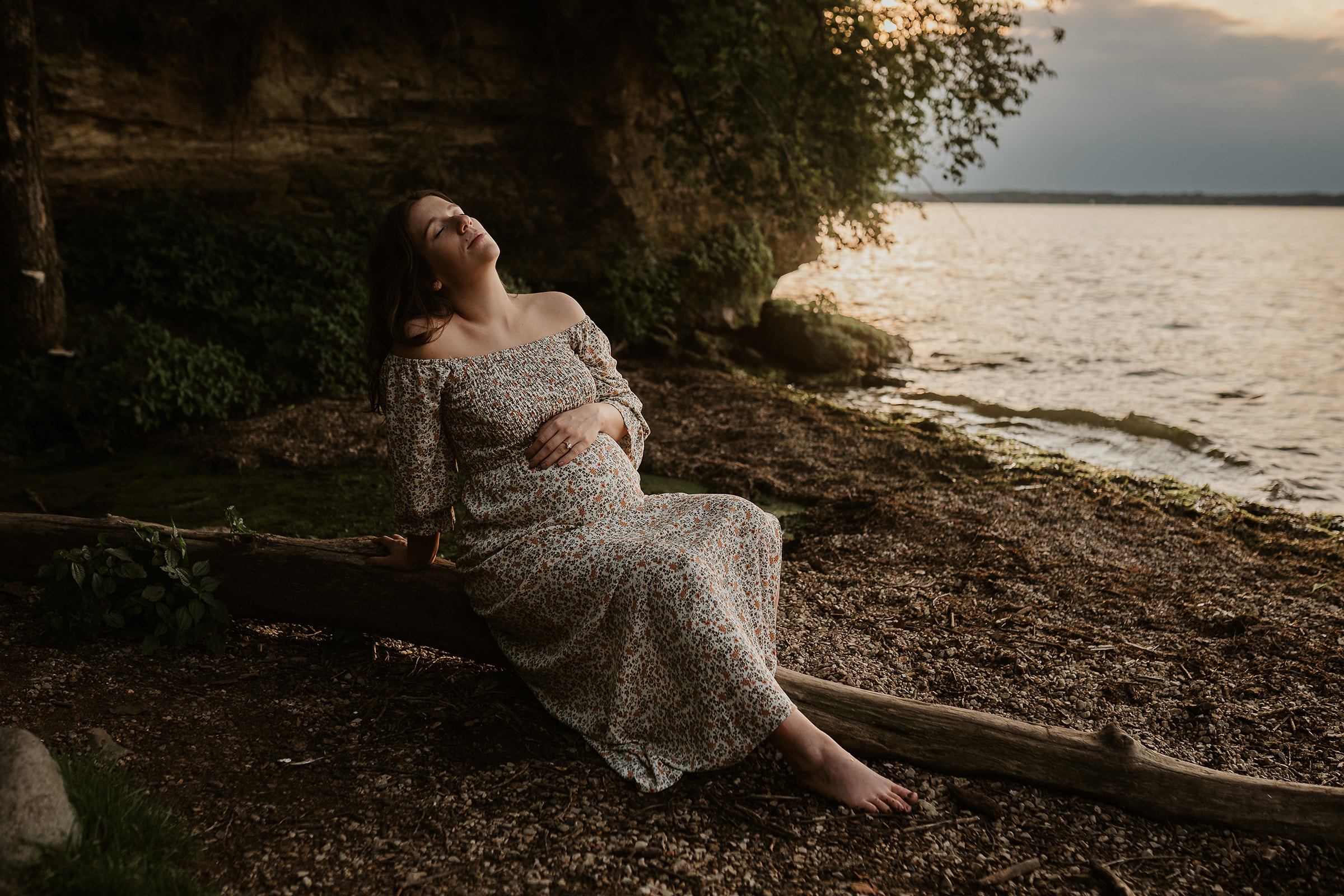 Pregnant woman sitting near the lake during sunset for a maternity session