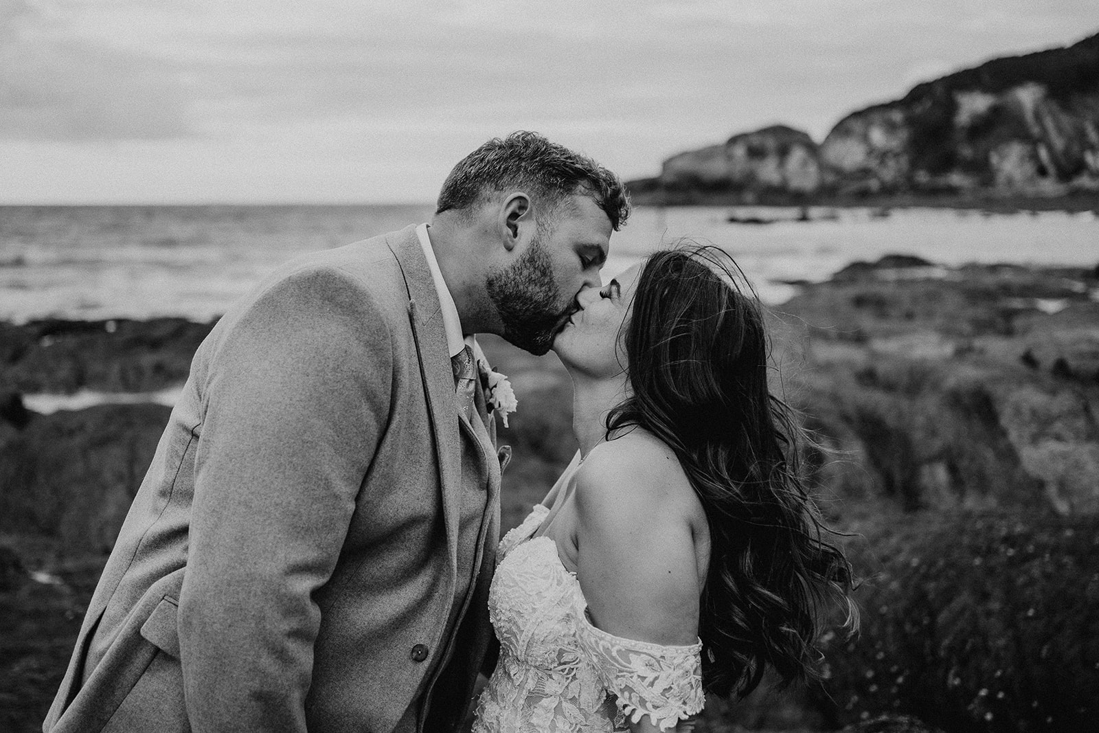 Black and white photo of newlywed couple kissing on the beach at their Sandy Cove Hotel wedding