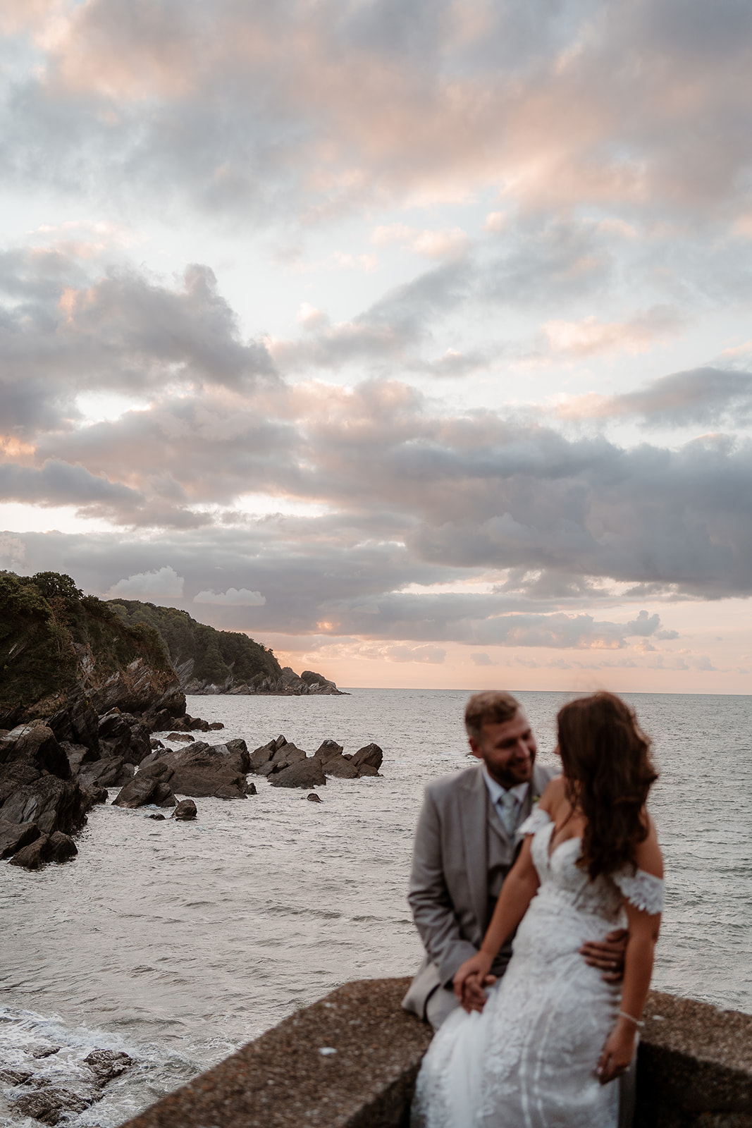 Bride and groom cuddle in the foreground with the pink cloudy sunset sky behind them - Sandy Cove Hotel wedding