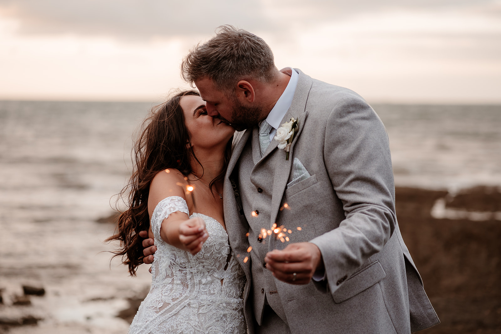 Bride and groom kiss while holding sparklers on the beach at their Sandy Cove Hotel wedding