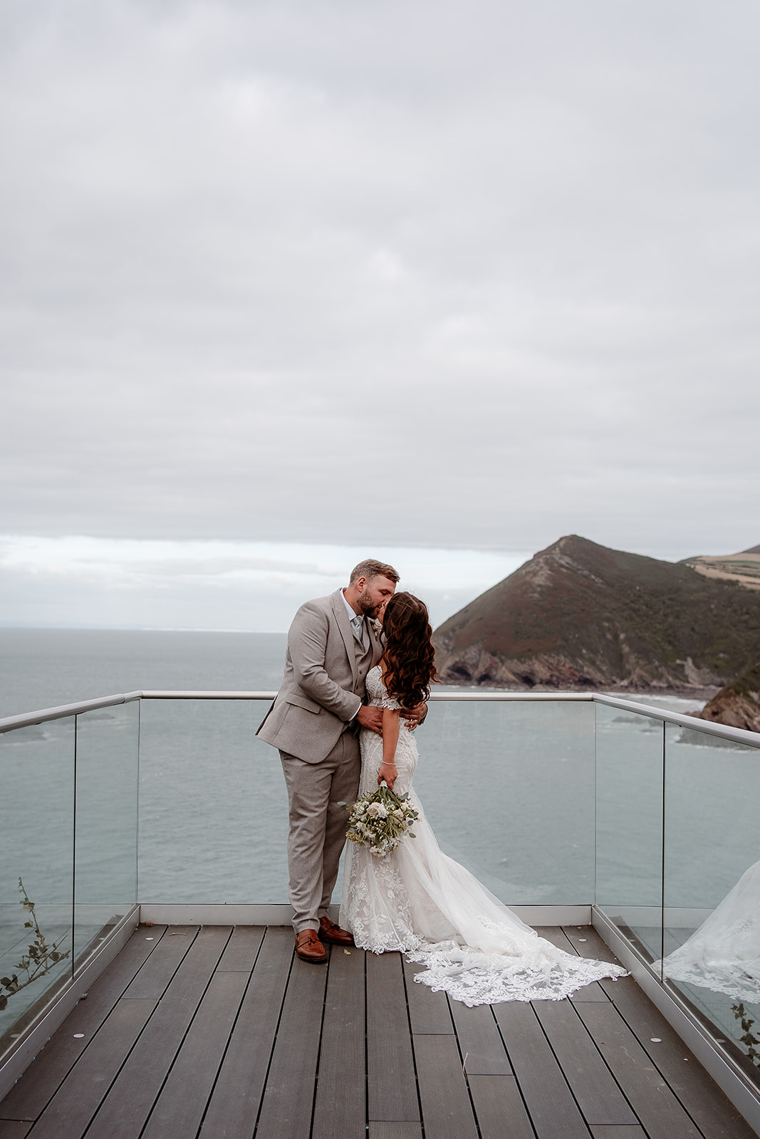 A bride and groom kiss on the platform overlooking the sea at their Sandy Cove Hotel wedding