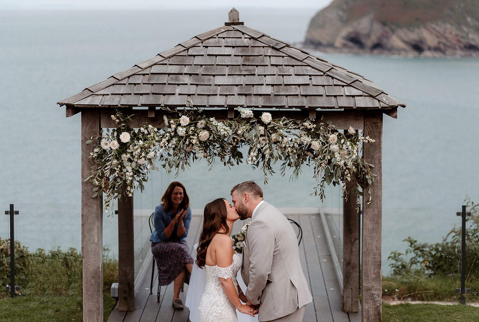 Bride and groom share their first kiss under the floral arch at their outdoor Sandy Cove Hotel wedding