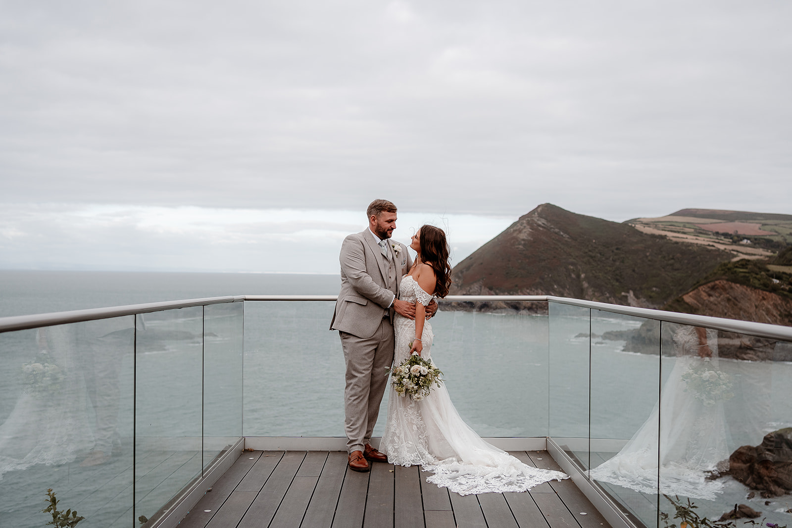 A bride and groom snuggle together on the platform overlooking the sea at their Sandy Cove Hotel wedding