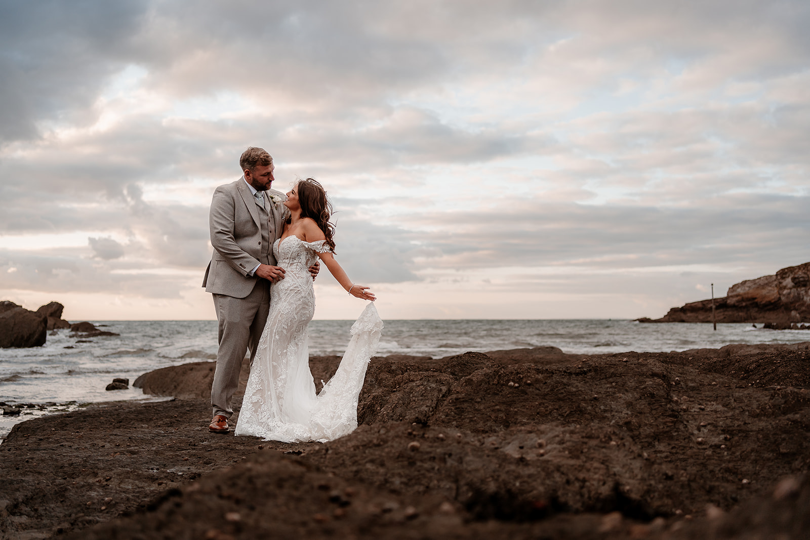 Couple on the beach with a moody sunset sky behind them at their Sandy Cove Hotel wedding