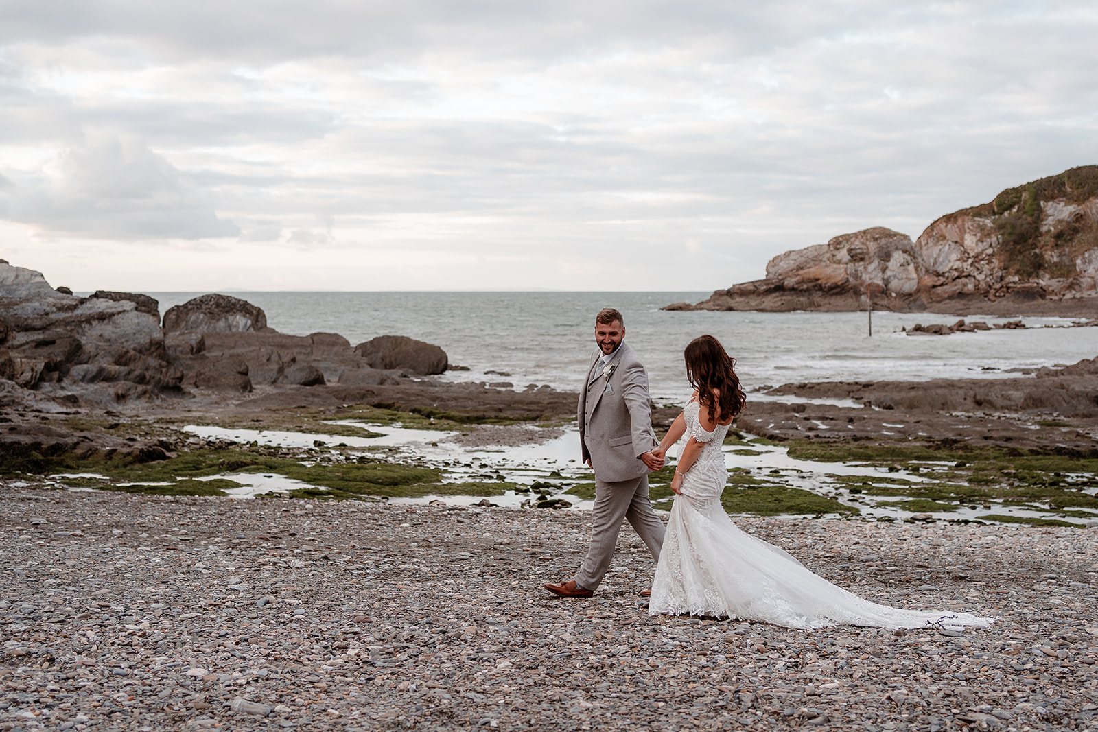 Couple walk hand in hand by the sea at their Sandy Cove Hotel wedding